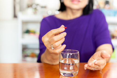 Senior woman hands holding tablet with glass of water on table.の写真素材