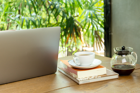 Laptop computer and cup of coffee with book on wooden table in cafe.の写真素材