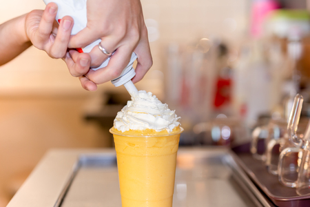 Hand squeezing cream on glass of orange smoothie drink.の写真素材