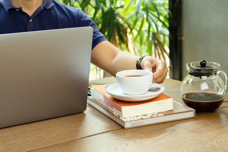 Businessman holding cup of coffee while working on laptopの写真素材
