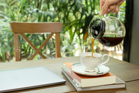 Man pouring coffee into a cup with laptop on the tableの写真素材