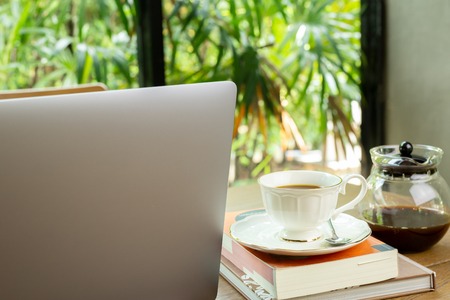 Laptop computer and cup of coffee with book on wooden table in cafeの写真素材