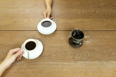 Top view hand holding a cup of coffee with coffee pot on wooden tableの写真素材