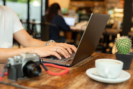 Male hands typing on laptop keyboard with camera and coffee on table.の写真素材
