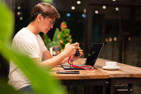 Man holding digital mirrorless camera checking photo with laptop on the table.の写真素材