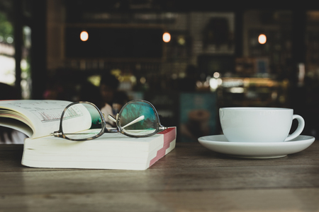 Eyes glasses on book with cup of coffee on wooden desk in blurの写真素材