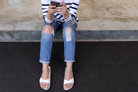 Woman in rip jeans looks at mobile phone.の写真素材