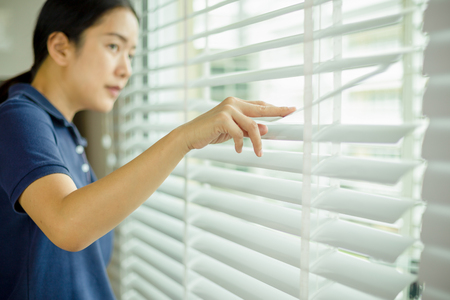Curious asian woman looking through window blind.の写真素材