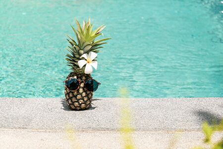 Funny pineapple with sunglasses and flower next to swimming pool.の写真素材