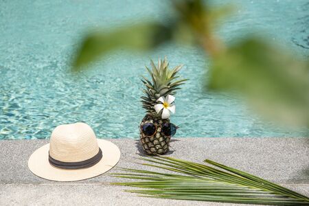 Funny pineapple with sunglasses and flower and hat by swimming pool.の写真素材