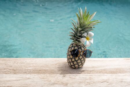 Funny pineapple in sunglasses with plumeria flower near swimming pool.の写真素材