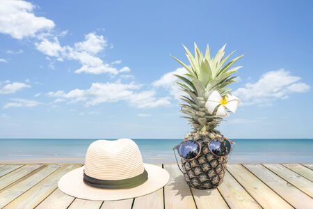 Pineapple with sunglasses and flower on wooden floor near the beach.の写真素材
