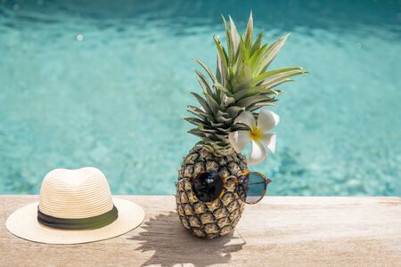 Funny pineapple in sunglasses with plumeria flower and hat near swimming pool.の写真素材
