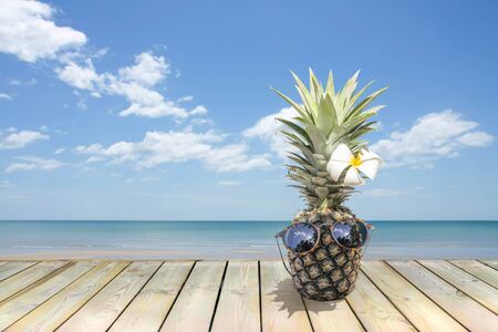 Pineapple with sunglasses and flower on wooden floor next to the beachの写真素材