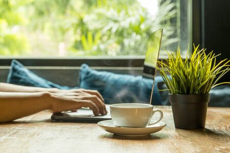 Selected focus cup of coffee with businessman typing on the keyboard laptop.の写真素材