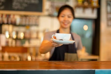 Asian woman barista serving coffee cup to customer at cafe.の写真素材