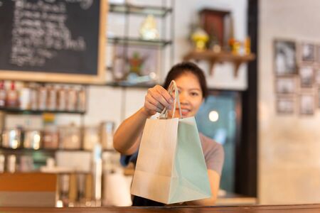 Waitress at counter giving eco friendly paper bag with take away drink in cafe.の写真素材
