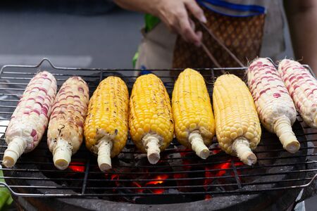 Street food man grill corn on the cob on the hot stove with charcoal.の写真素材