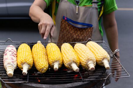 Street food woman grill corn on the cob on the hot stove with charcoal.の写真素材