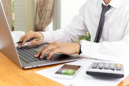 Businessman working on laptop with paperwork on table.の写真素材