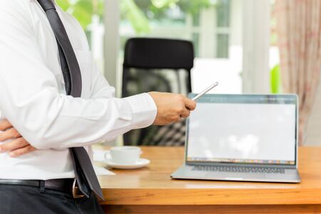 Businessmans hand holding cellphone with laptop on wooden desk.の写真素材