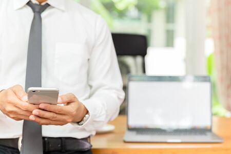 Businessmans hand holding cellphone with laptop on wooden desk.の写真素材