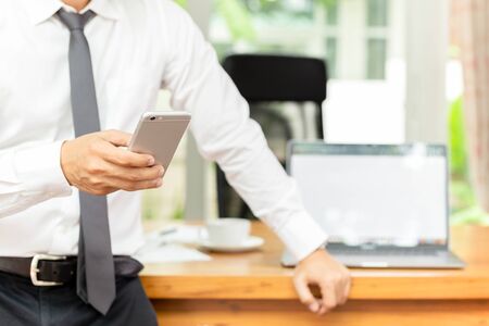 Businessmans hand holding cellphone with laptop on wooden desk.の写真素材