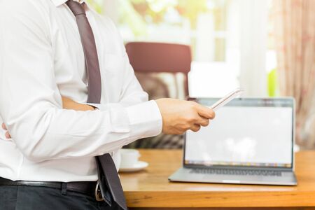 Businessmans hand holding cellphone with laptop on wooden desk.の写真素材