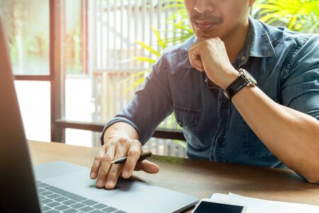 Man working on laptop with cell phone on wooden desk.の写真素材