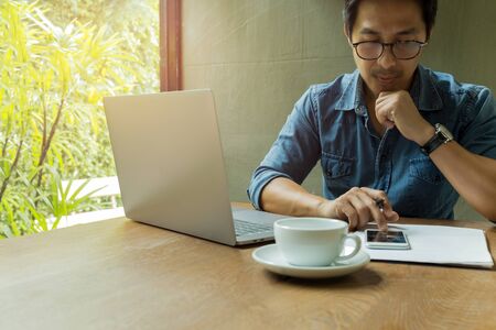 Businessman using cell phone with laptop and coffee cup on wooden desk.の写真素材