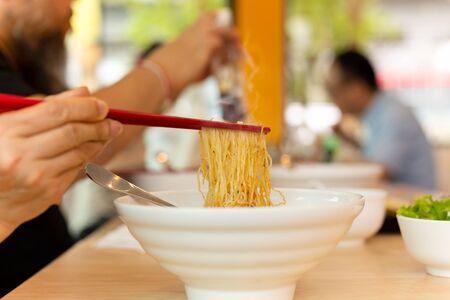 Woman eating egg noodles with chopsticks on wooden table.の写真素材