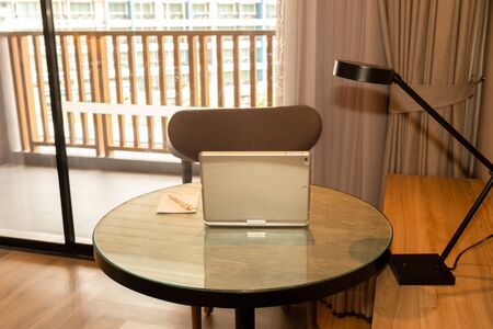 Laptop with pen and paper on table in hotel room.の写真素材