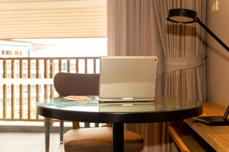 Laptop with pen and paper on table in hotel room.の写真素材