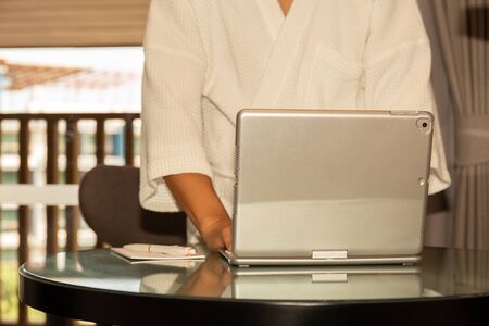 Businessman in bathrobe working on laptop in hotel room.の写真素材