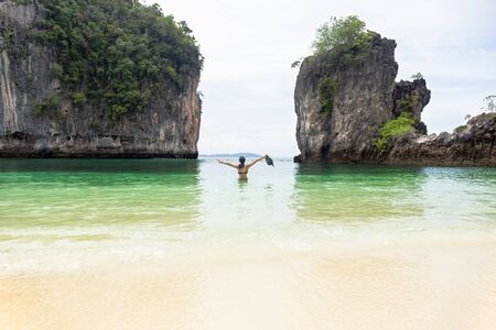 Woman standing in the sea and hands up holding beach hat on vacation.の写真素材