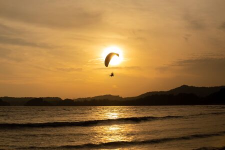 Beautiful Silhouette of paraglider flying in the sky of sunset on the beach.の写真素材