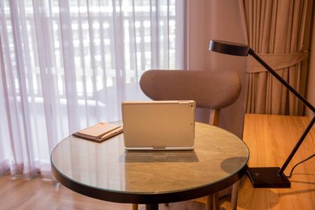 Laptop with pen and paper on table in hotel room.の写真素材
