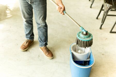 Man worker with mop and bucket cleaning floor in the cafe.の写真素材