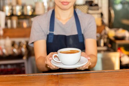 Waitress serving coffee while standing in coffee shop counter.の写真素材
