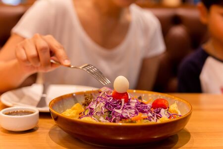 Woman hand with fork eating salad with tomato and quail egg in a plate.の写真素材