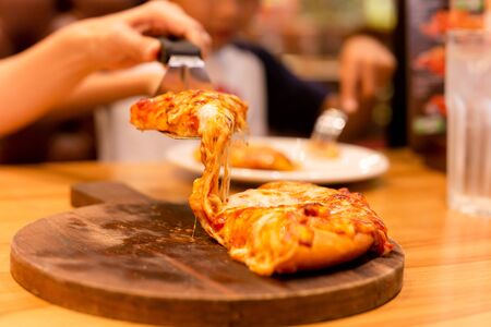 Female hand taking a slice of pizza from wooden tray.の写真素材