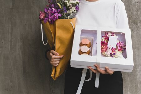 Woman holding flowers and gift box on grey background.の写真素材
