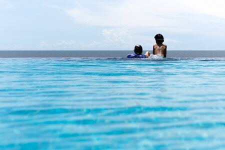Mother and young son relax in swimming pool looking over the ocean on summer vacation.の写真素材
