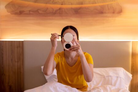 Woman applying make up sitting on the bed.の写真素材