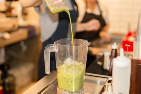 Barista pouring matcha green tea into blender make smoothies in cafe.の写真素材