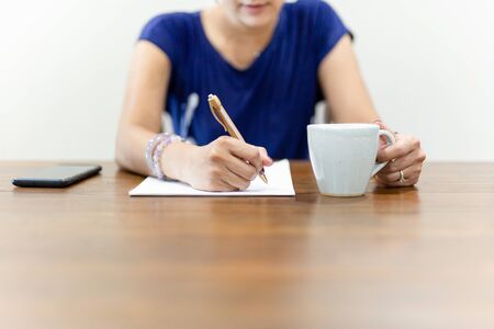 Businesswoman hand writing on paperwork with cup of coffee on working desk.の写真素材