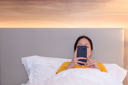 Woman using cell phone while lying in bed.の写真素材