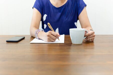 Businesswoman hand writing on paperwork with cup of coffee on working desk.の写真素材