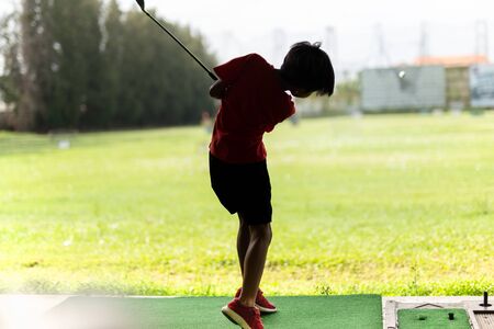 Young asian boy is practicing his golf swing at the golf driving range.の写真素材