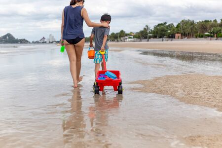 Mother and son walking on the beach with beach toys on summer vacation.の写真素材